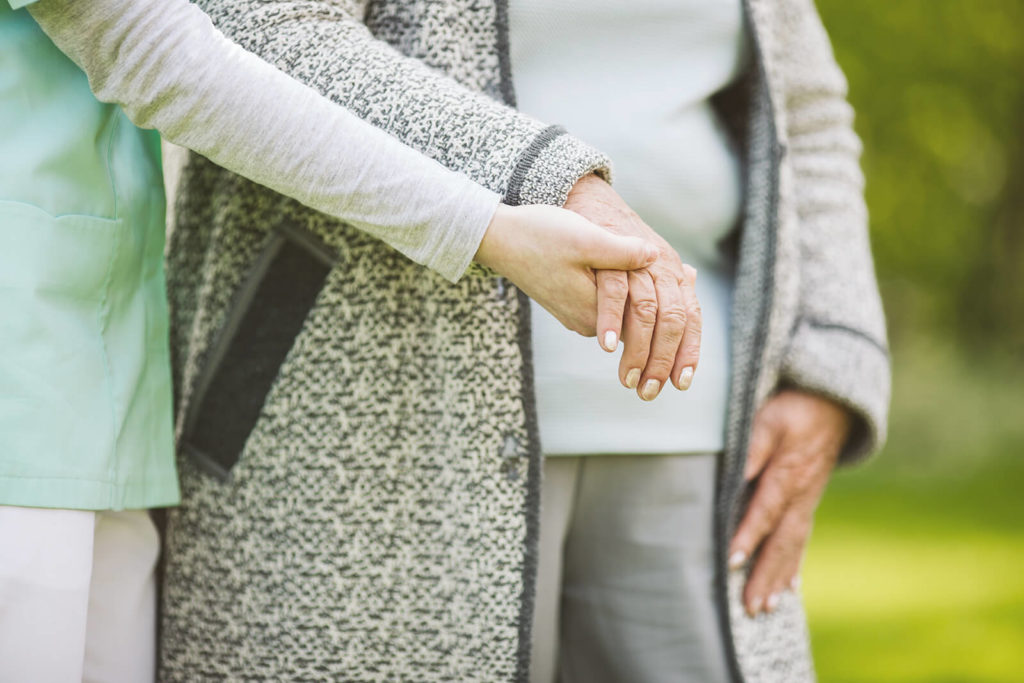 A caregiver holding the hands of a senior woman using a walker